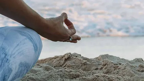 Meditasjonsstilling på strand med hav i bakgrunnen og teksten «mediyoga på bygdøy».