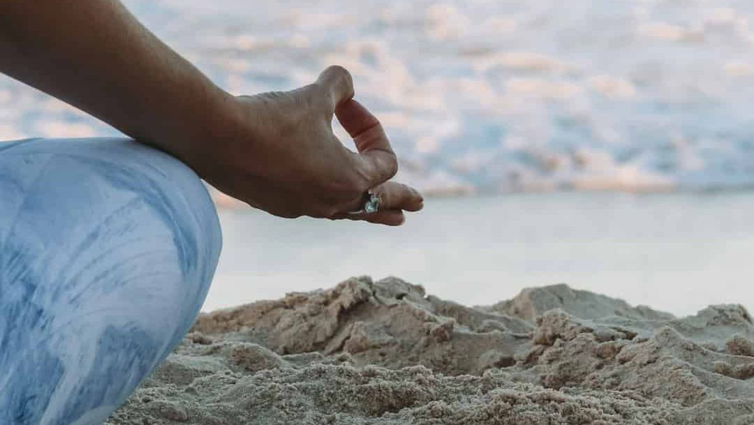 Meditasjonsstilling på strand med hav i bakgrunnen og teksten «mediyoga på bygdøy».